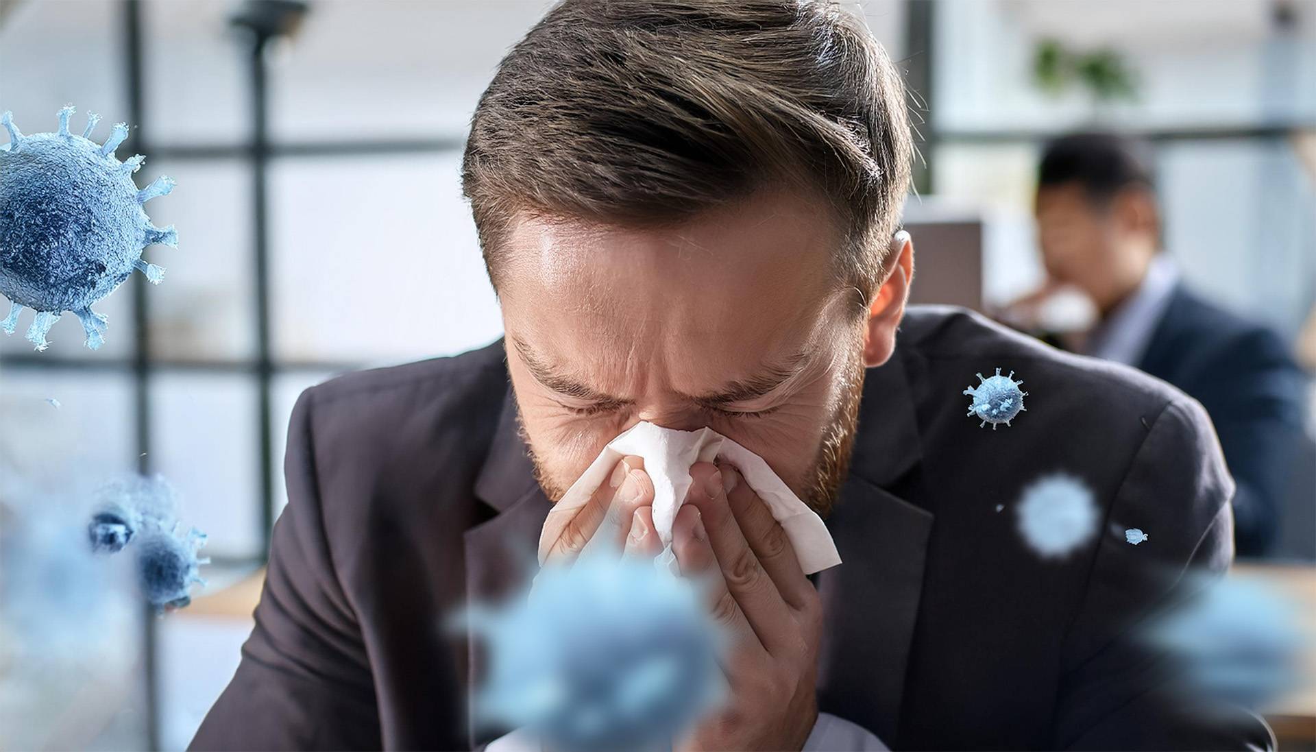 A man in an office is cleaning his nose. Around him are illustrated viruses.