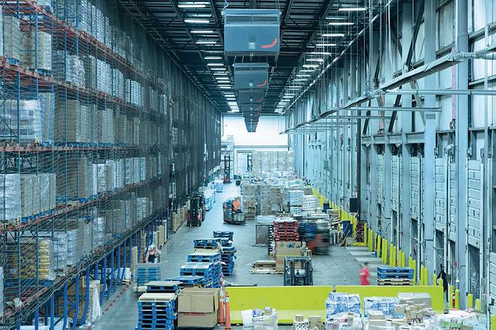 Large high-bay warehouse with pallets, forklift trucks and industrial air cleaners on the ceiling.
