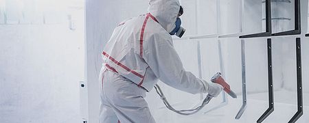 Worker coating metal pieces with spray paint