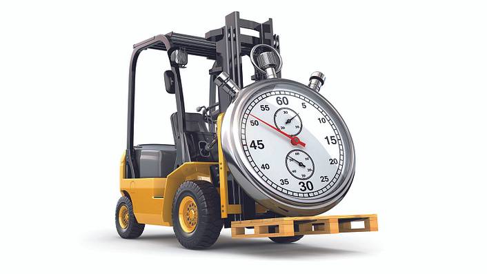 A forklift truck carries a pallet with a large stopwatch on it.