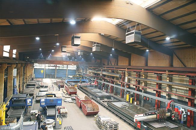 A large industrial hall with machines, pallets and a modern air filtration system.