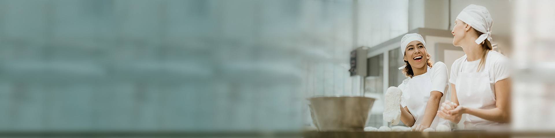 Two female bakers smiling with dough in their hands