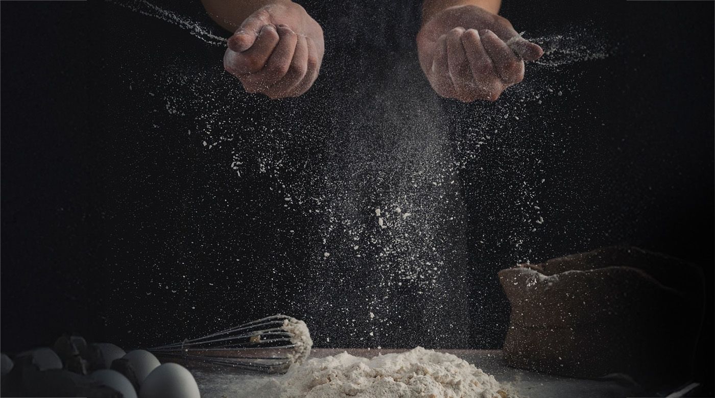 Zwei Hände bereiten einen Teig zu, wodurch viel Mehlstaub entsteht.