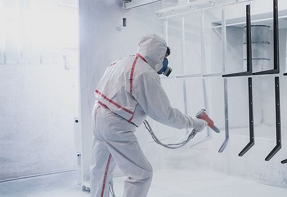 Worker coating metal pieces with spray paint