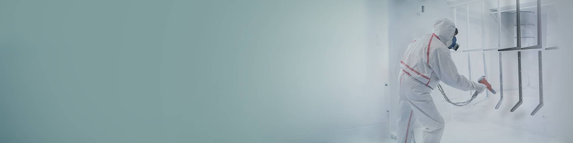 Employee in protective clothes coating components with spray paint