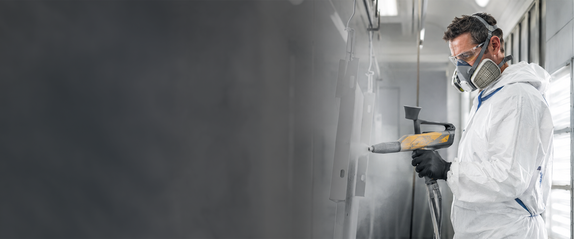 Coating & surface technology – air quality warning Worker in a white protective suit and respirator mask spray-painting a wall inside a coating booth