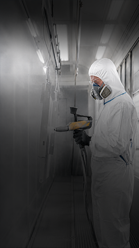 Coating & surface technology – air quality warning Worker in a full protective suit and respirator spray-painting inside a coating booth corridor
