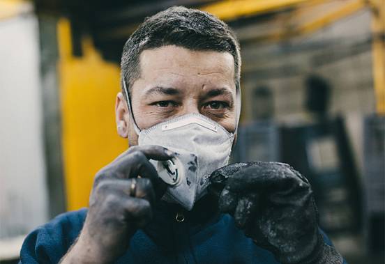 Industrial worker with protective mask and dirty hands in a factory hall.