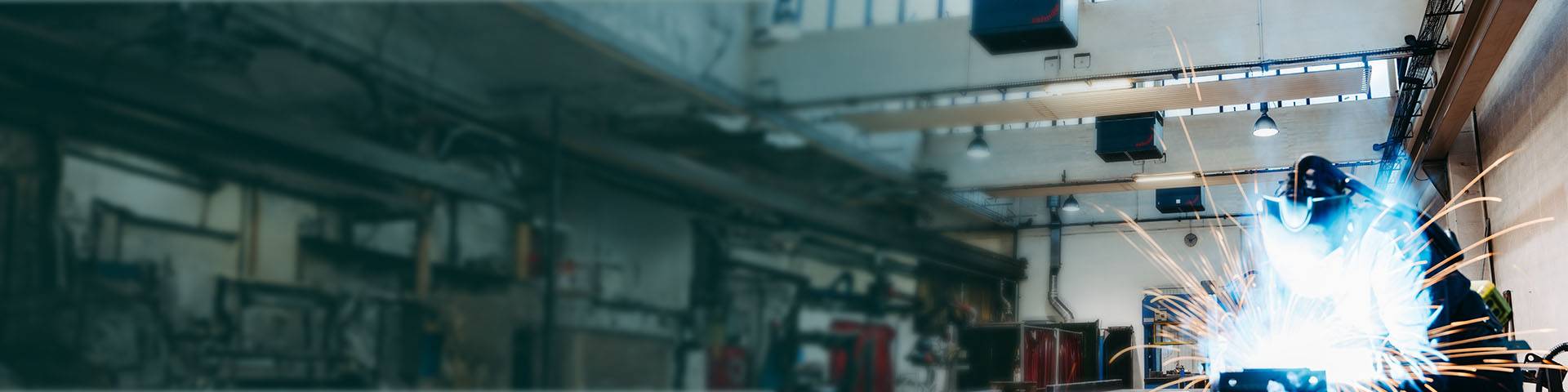Welder in an industrial hall with flying sparks during metalworking.
