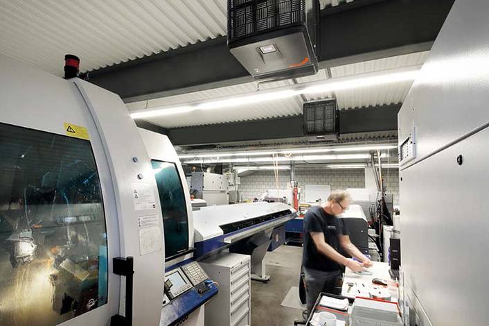 Industrial air purifier in a modern manufacturing facility with employees in a highly automated production hall.