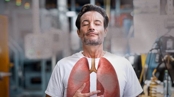 A man breathes in dirty air. A lung is depicted on his chest, in which the dirty dust is deposited.