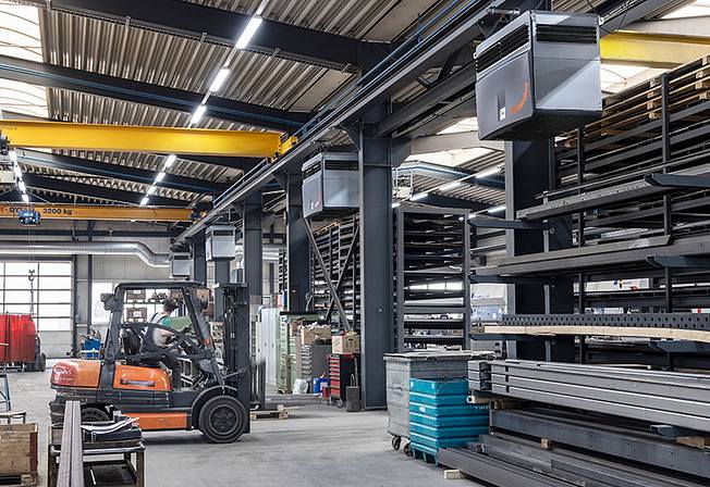 An employee drives a forklift truck into a warehouse for metal parts, which is equipped with industrial air purifiers.