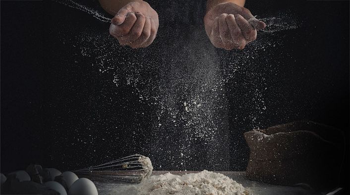 Zwei Hände bereiten einen Teig zu, wodurch viel Mehlstaub entsteht.