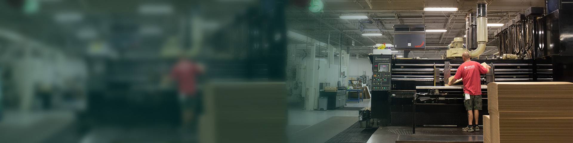 An employee at an industrial machine processes cardboard material in a production hall.