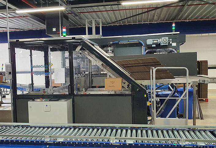 Automated packaging machine with conveyor belt in a production hall.