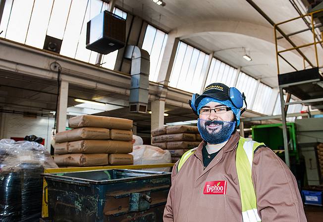 Warehouse worker with protective clothing, ear defenders and beard protection in a production hall with stacked sacks.