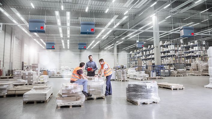 Mitarbeiter beraten sich in einer Lagerhalle, welche mit Luftreinigern von Zehnder Clean Air Solutions ausgestattet ist.