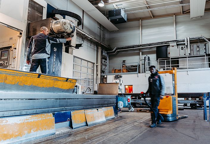 Industrial production hall with employees at a large machine and transport trolley.
