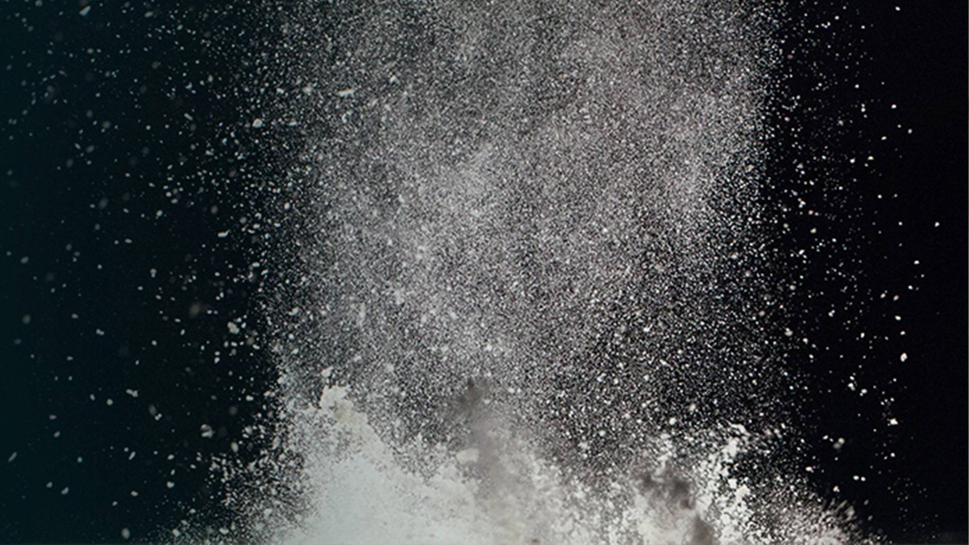 Fine silica dust particles swirl through the air against a dark background.