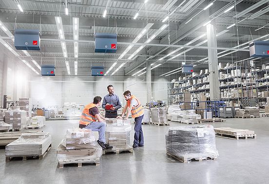 In a warehouse equipped with Zehnder Clean Air Solutions industrial air cleaners, employees meet.