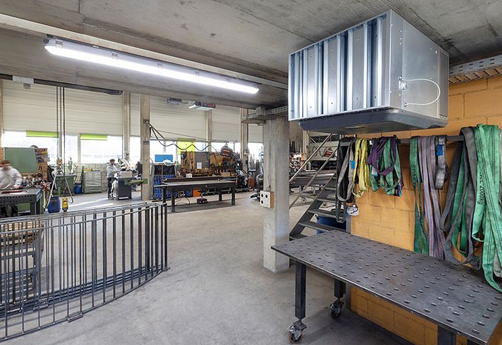 Metal workshop with welding table, lifting straps and industrial air cleaners.