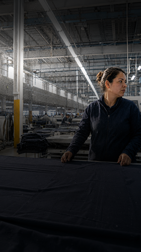 Textile industry – air quality warning Worker standing in a dimly lit textile factory with rows of machines in the background