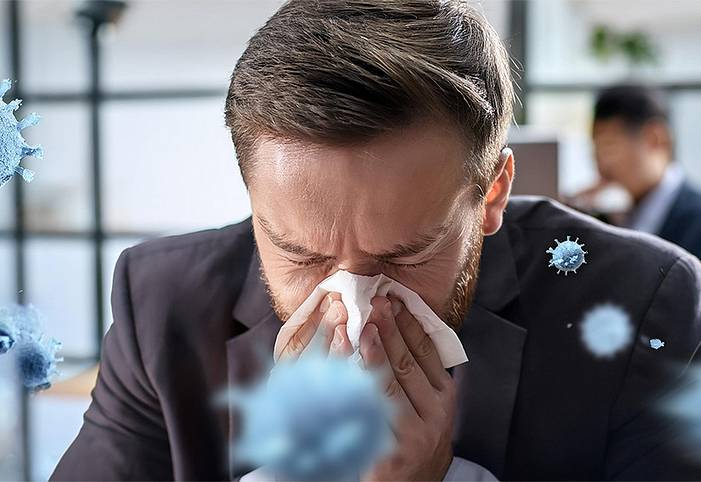 A man in an office is cleaning his nose. Around him are illustrated viruses.