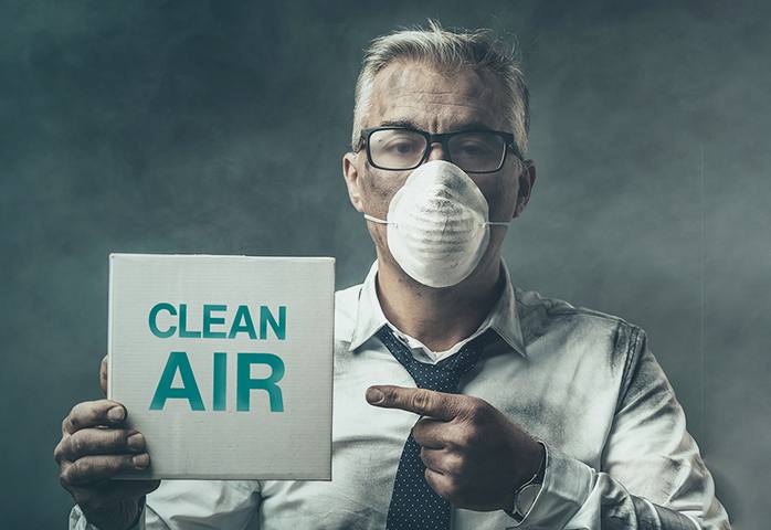 A dirty man with a protective mask holds a sign saying “Clean Air”.
