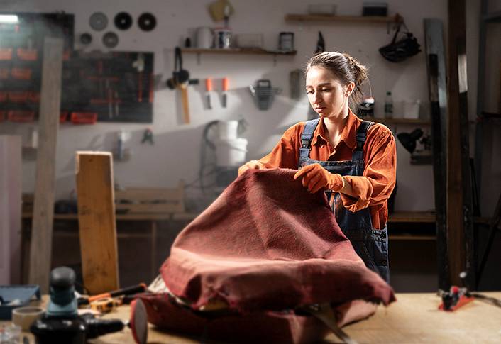 Eine Mitarbeiterin steht in einer Schreinerei und betrachtet ein Stück Stoff auf einer Werkbank.