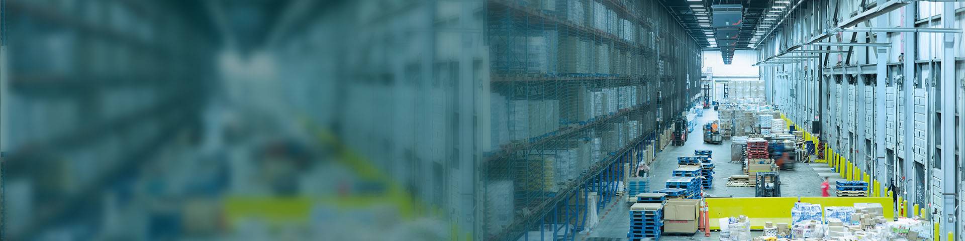 Large high-bay warehouse with pallets, forklift trucks and industrial air cleaners on the ceiling.