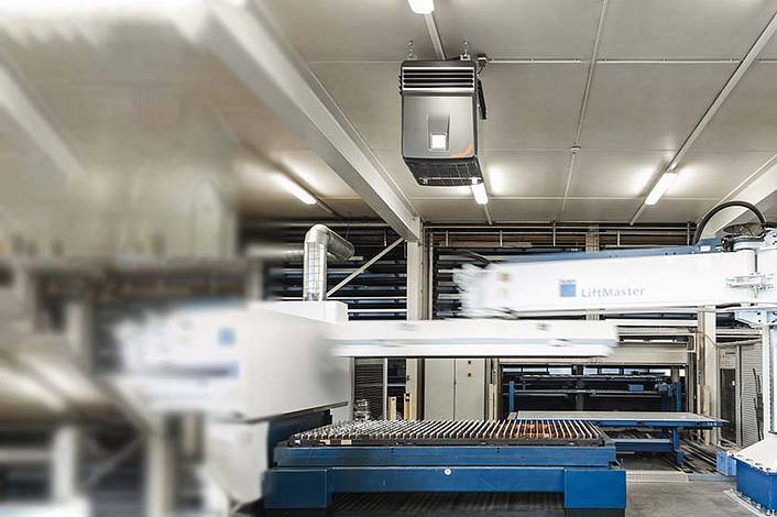 An industrial air purifier is suspended above an automated production line in a factory building.