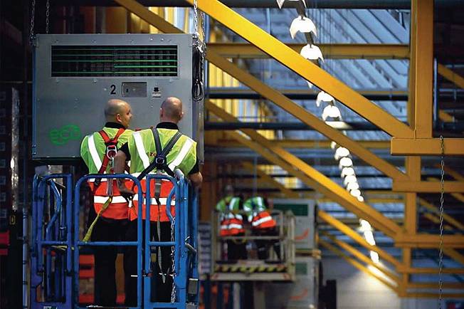 Two employees in high-visibility waistcoats attach an industrial air purifier to the ceiling.