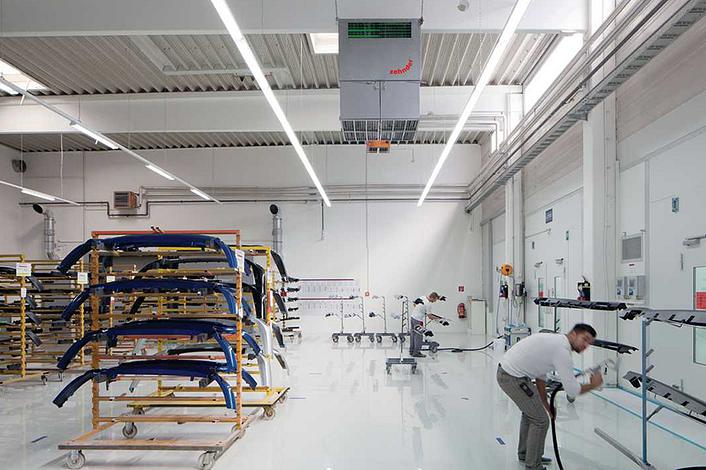 Employees spray car parts in a hall with air purifiers.