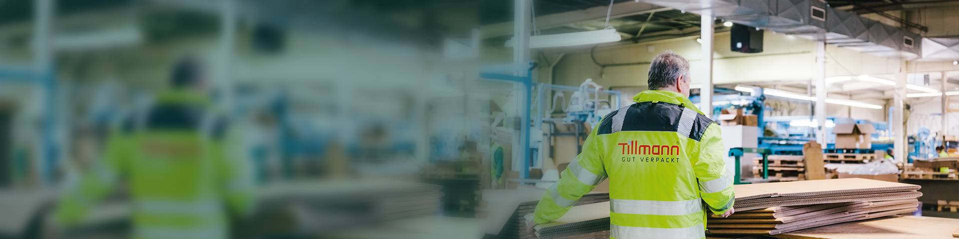 An employee in a high-visibility jacket stacks folded cardboard boxes on top of each other.