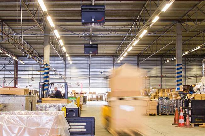 Industrial air purifiers hang from the ceiling of a logistics hall.