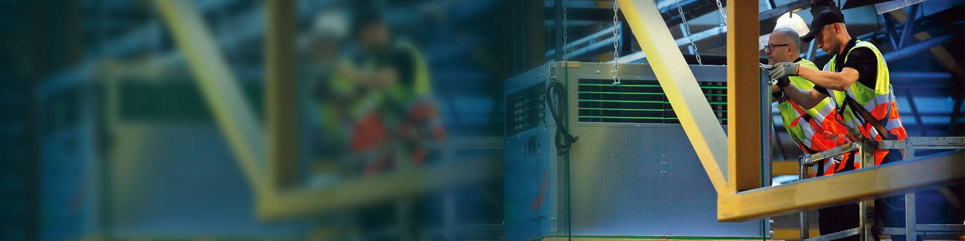Two employees in high-visibility waistcoats attach an industrial air purifier to the ceiling.